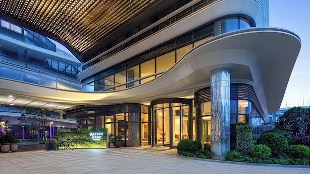 Un hotel moderno con fachada curva, amplias ventanas de vidrio y una entrada bien iluminada.