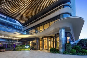 Egy modern hotel, ívelt homlokzattal, nagy üvegablakokkal és jól megvilágított bejárattal.