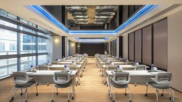 A conference room with rows of tables and chairs, large windows, and a modern ceiling design.