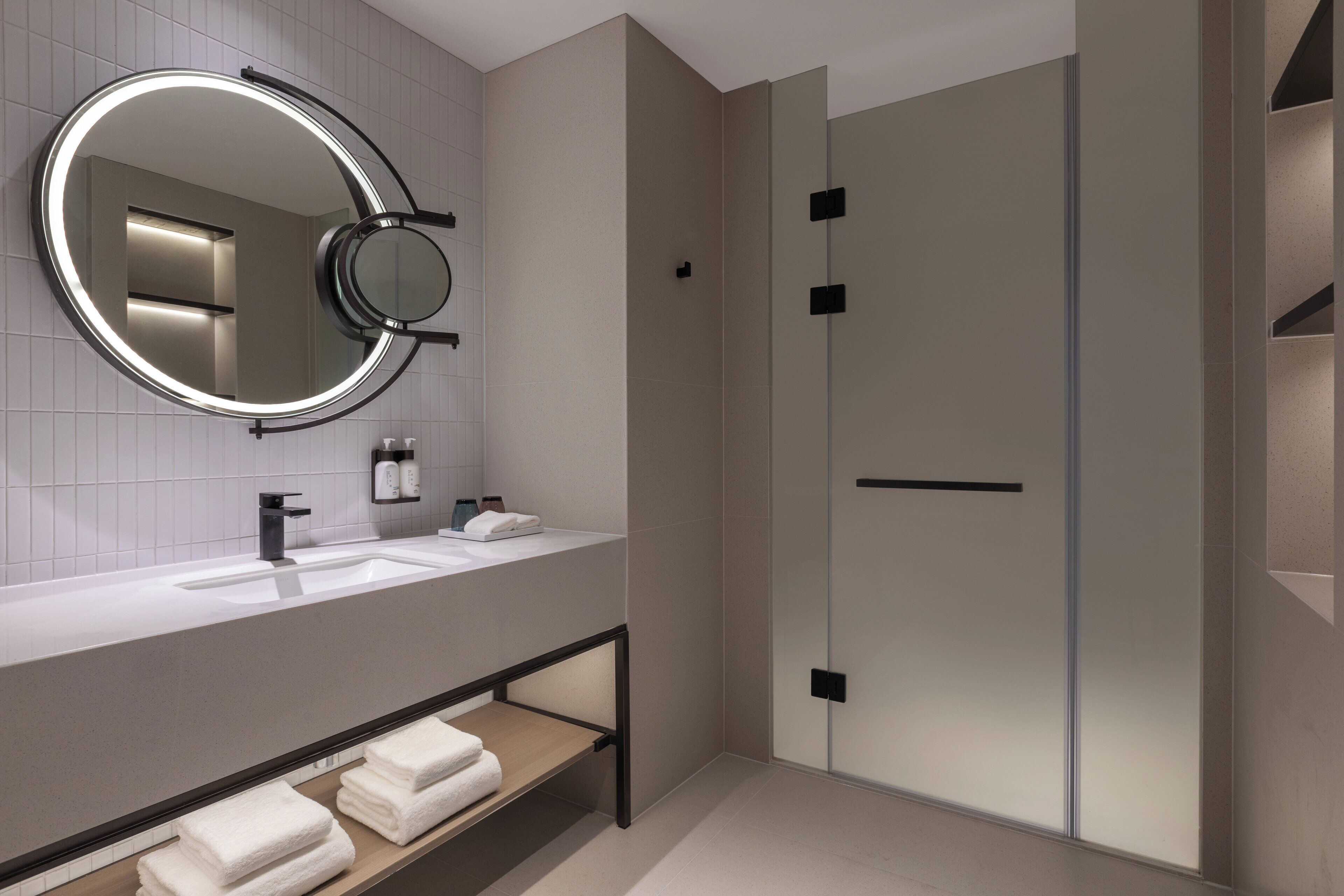 A modern bathroom with a round mirror, a sink, and a shower area.