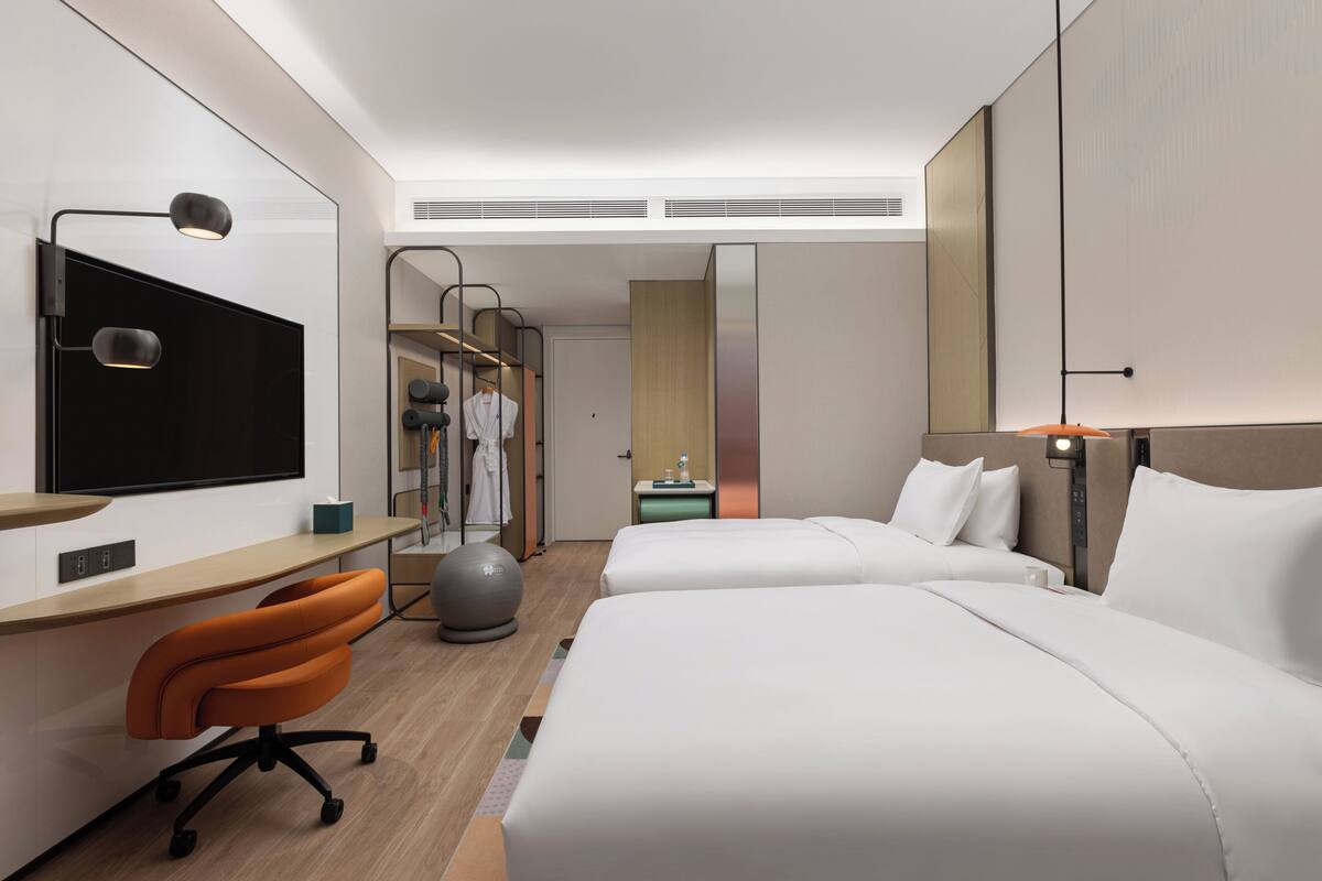 Ein modernes Hotelzimmer mit zwei Betten, einem Schreibtisch, einem Stuhl, einem Fernseher und einem Trainingsball.