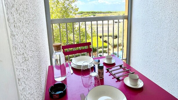 Ein Balkon mit Tisch für zwei Personen, einem Stuhl und Blick auf Grünflächen und einen klaren Himmel.