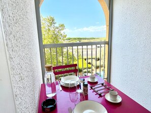 Un balcon avec une table dressée pour deux personnes, une chaise et une vue sur la verdure et un ciel dégagé.