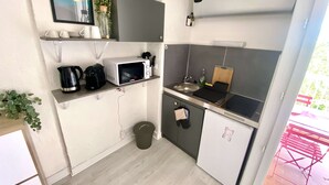 Eine kompakte Küche mit Mikrowelle, Spüle und kleinem Kühlschrank. Regale mit Geschirr und ein Topf mit Pflanze.