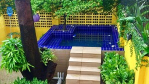 A blue tiled pool with a wooden staircase leading up to it, surrounded by greenery and yellow walls. - Cosmopolitan Hostel (Recife)