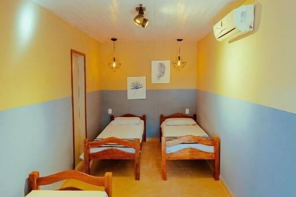 A room with two wooden beds, a ceiling fan, an air conditioning unit, and a wall-mounted light fixture.
