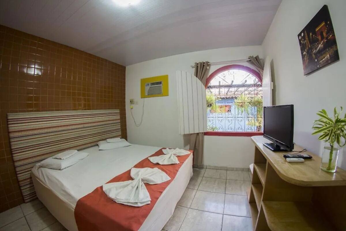 A hotel room with a bed, a TV, a desk, and a window with curtains.
