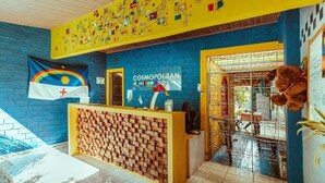 A reception area with a blue brick wall, a yellow ceiling, and a sign reading "COSMOPOLITAN HOSTS". - Cosmopolitan Hostel (Recife)