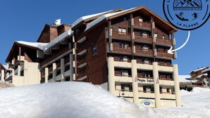 A multi-story hotel with balconies, a ski slope in the background, and a logo indicating it's a ski resort. - Le balcon du soleil, Pied de pistes 2100m 5 pers, Plagne Soleil, heart of the resort (La Plagne-Tarentaise)