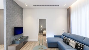 A modern living room with a flat-screen TV, a blue sofa, and a small coffee table. - Domus Augustea - Cesare 4 (Rome)