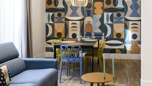 A modern living room with a blue sofa, a dining table with chairs, and a geometric patterned wall. - Domus Augustea - Cesare 4 (Rome)