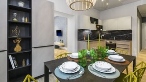 A modern dining area with a dark table set for four, surrounded by yellow chairs, and a kitchen in the background. - Domus Augustea - Cesare (Rome)