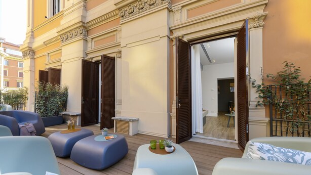 A terrace with modern seating, a small table with drinks, and a door leading to an interior space. - Domus Augustea - Cesare (Rome)