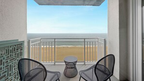 Ein Balkon mit zwei Stühlen und einem kleinen Tisch mit Blick auf einen Strand.
