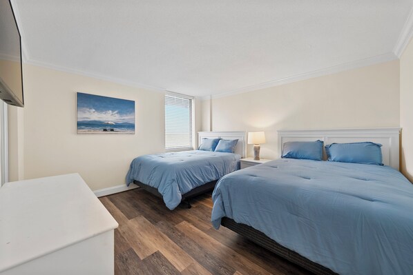 Een slaapkamer met twee bedden, een nachtkastje met een lamp, een schilderij aan de muur en een witte dressoir.