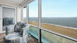 Ein Balkon mit Blick auf den Strand, ein Stuhl und eine Tür mit Fensterglas.