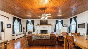 Amplia sala de estar con techo de madera, chimenea, sofá y comedor con mesa y sillas de madera.