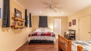 Un dormitorio con cama, piso de madera, ventilador de techo, una puerta y una silla.