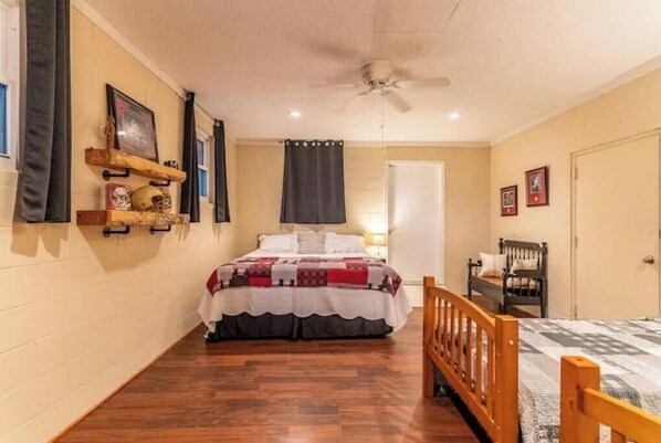 A bedroom with a bed, wooden floor, a ceiling fan, a door, and a chair.