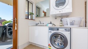 Un espace buanderie comprenant un lave-linge à chargement frontal, un sèche-linge, un évier et un miroir.