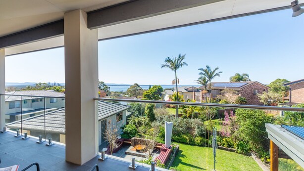 Un balcon donnant sur un quartier résidentiel, avec vue sur des maisons et une étendue d’eau.