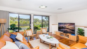 Ein modernes Wohnzimmer mit großem Fernseher, bequemen Sitzgelegenheiten und Blick ins Freie.