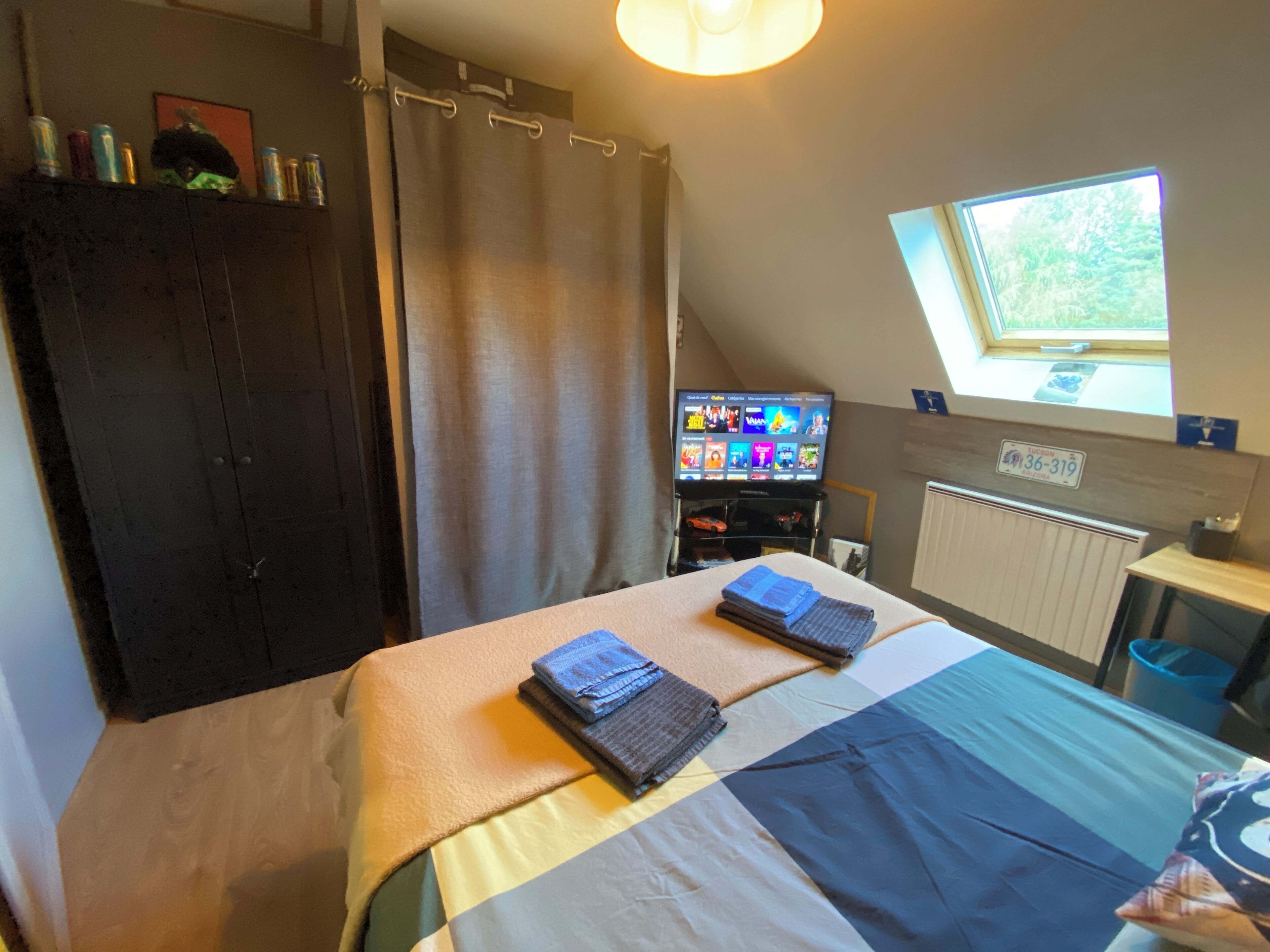 A bedroom with a bed, a TV, a window, and a radiator.