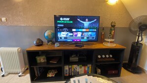A living room with a flat-screen TV displaying a sports channel, a globe, a clock, and a bookshelf. - "Private and corporate rentals. 3 bedrooms and sofa bed. (Le Vaudoué)