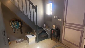 A staircase with a dark railing, a small table with a vase, a window with curtains, and a door with a decorative panel. - "Private and corporate rentals. 3 bedrooms and sofa bed. (Le Vaudoué)