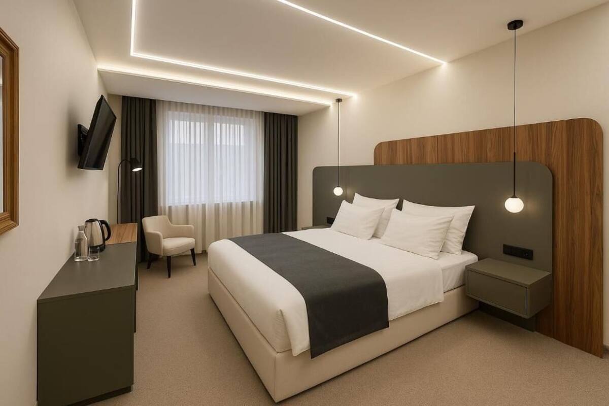 A modern hotel room with a large bed, bedside tables, a desk, a chair, and a TV mounted on the wall.