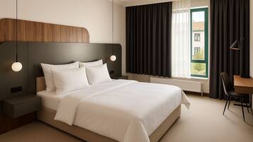 A modern hotel room with a large bed, a desk, and a view of the outside.