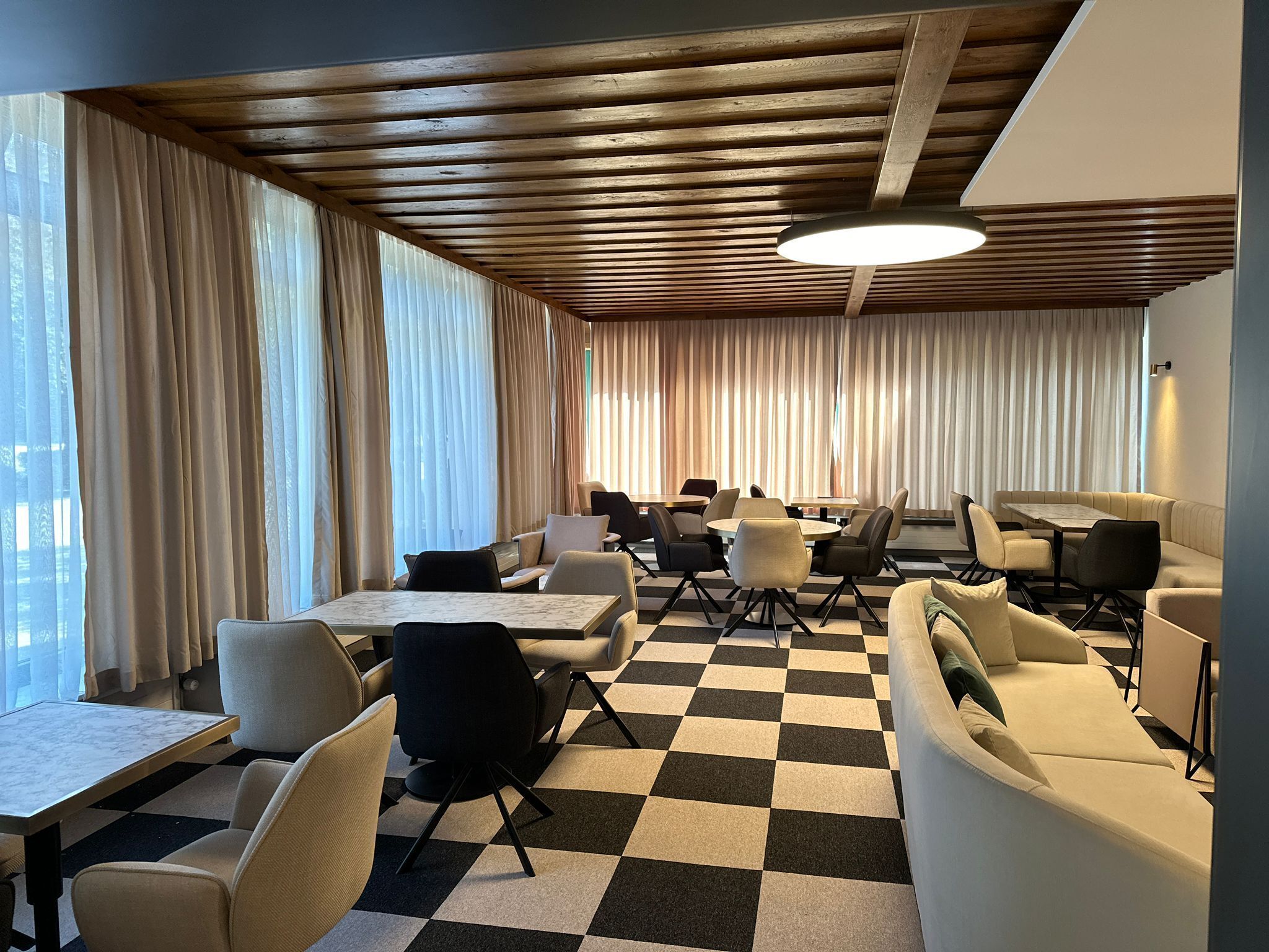 A modern interior with a checkered floor, wooden ceiling beams, and a mix of seating including tables and couches.