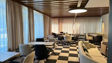 Ein modernes Interieur mit Schachbrettboden, Holzbalkendecke und einer Mischung aus Sitzgelegenheiten, darunter Tische und Couches.