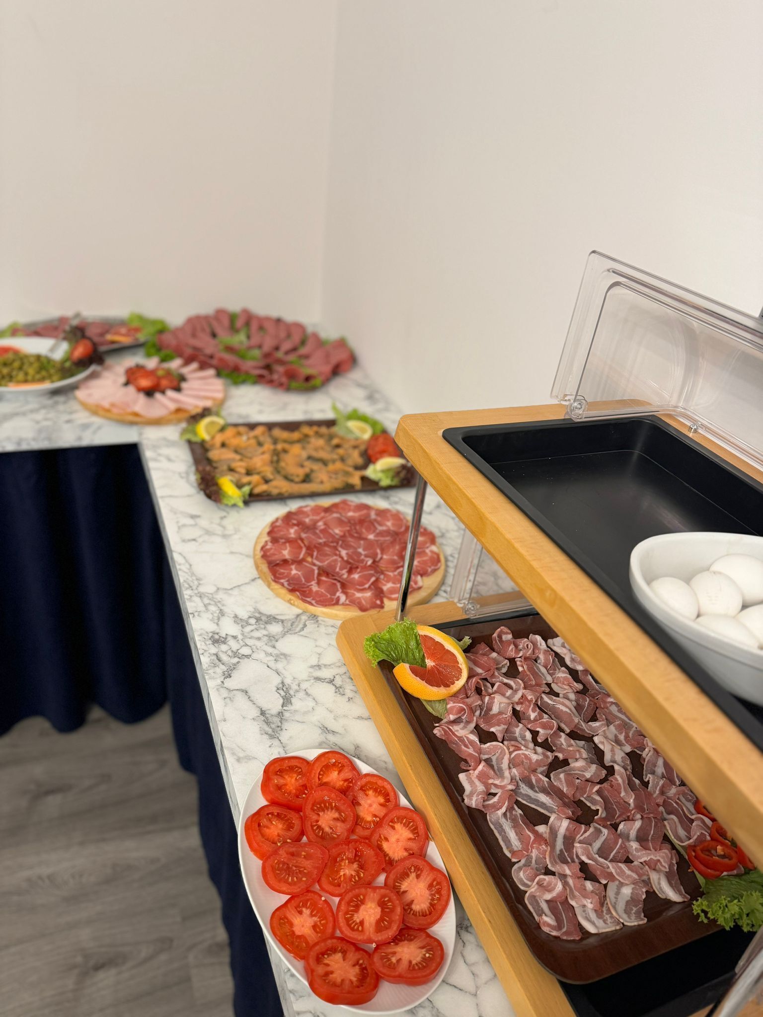 Una mesa de buffet con diversos alimentos, como carnes en rodajas, verduras y un bol de huevos.