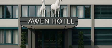 El exterior del Hotel Awen, con un diseño moderno, presenta dos estatuas de caballos en la entrada y una señalización clara sobre las puertas.