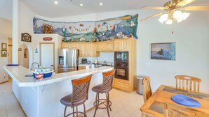 A kitchen with a central island, wooden cabinets, a refrigerator, an oven, and a dining area with a table and chairs. - Casa Vista -- Home with a View (Bullhead City)