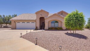 A single-story house with a garage, a small front porch, and a landscaped front yard with a tree and gravel pathway. - Casa Vista -- Home with a View (Bullhead City)