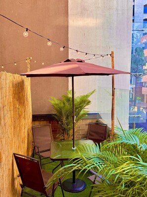 A patio area with a table and chairs, a string of lights, and a large umbrella. - 203-Oasis Urbano Con Terraza  (Bogotá)