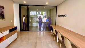 Um espaço moderno de coworking com uma longa mesa de madeira, cadeiras confortáveis e uma porta de vidro que dá para o exterior.