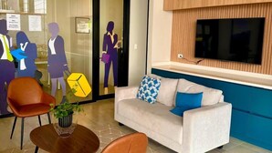 Um hall moderno com um sofá branco, duas cadeiras marrons, uma parede de destaque em madeira e uma televisão de tela plana.