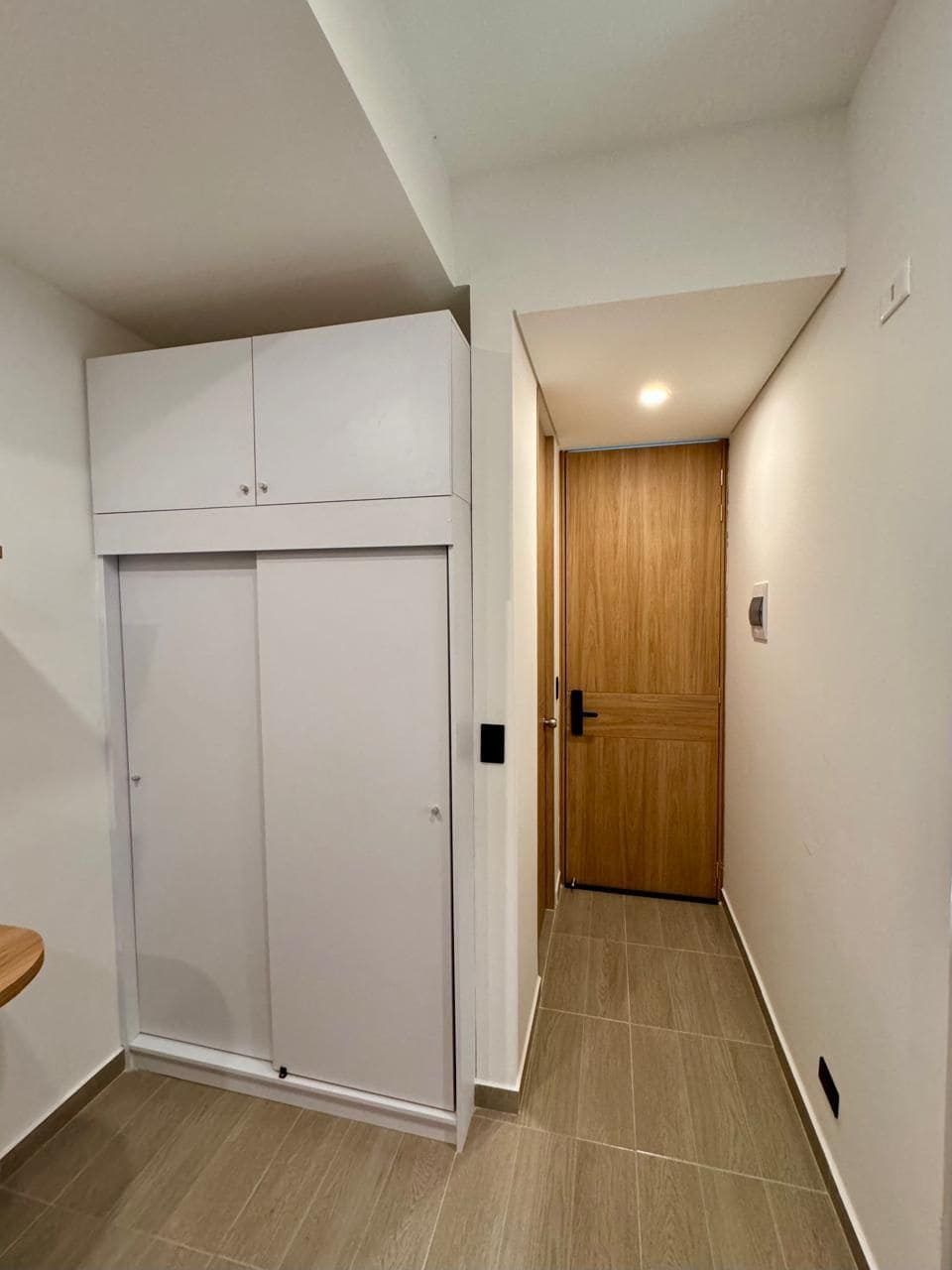 Un pasillo con un armario blanco, una puerta de madera y una pequeña mesa de madera.