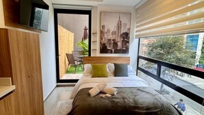 Quarto moderno com uma cama grande, guarda-roupa de madeira, pintura de paisagem urbana e vista para o exterior através de uma janela ampla.