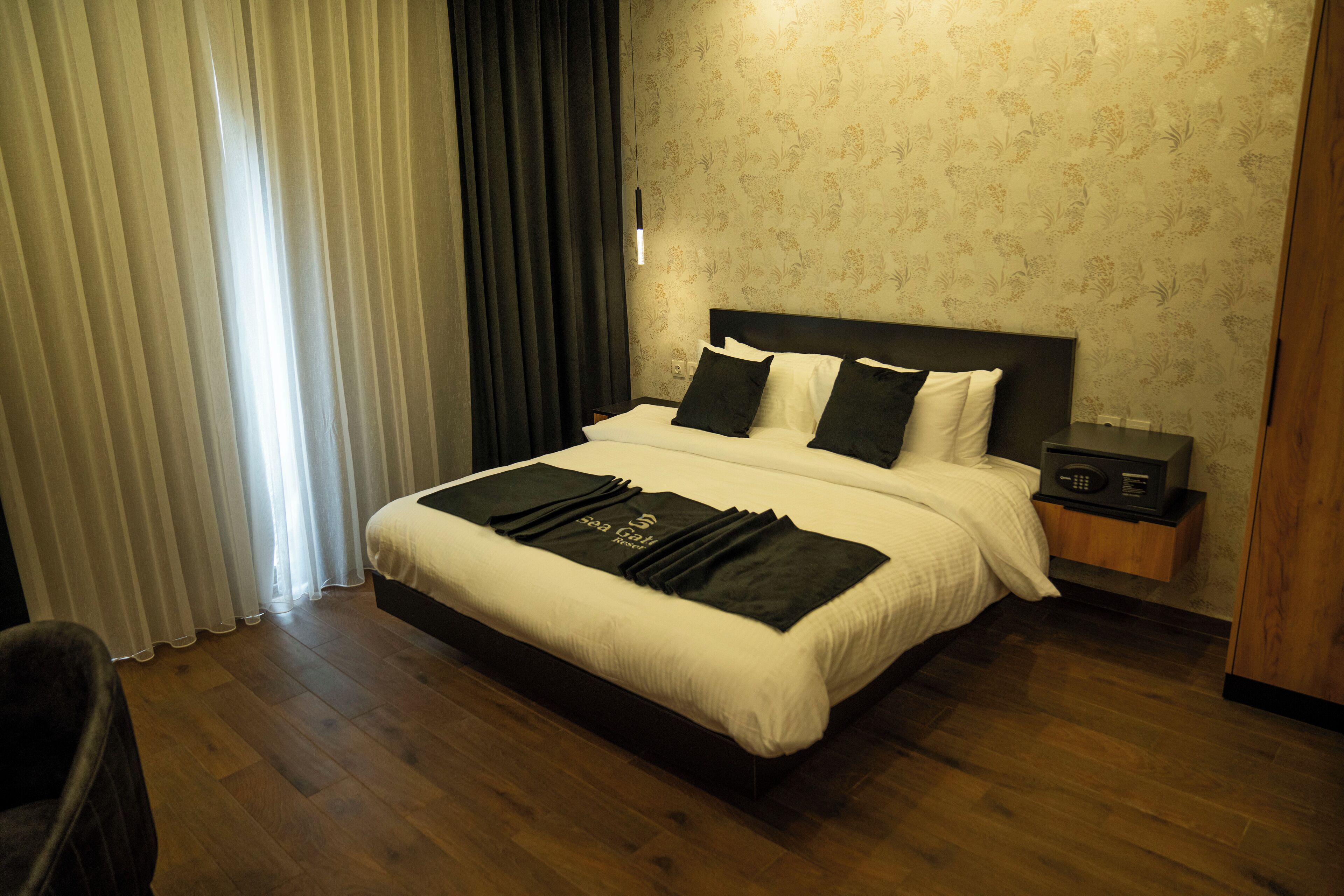 A neatly made bed with a black and white color scheme, a bedside table with a radio, and a window with curtains.