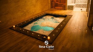 A spa area with a hot tub surrounded by candles, wooden flooring, and a tiled wall.