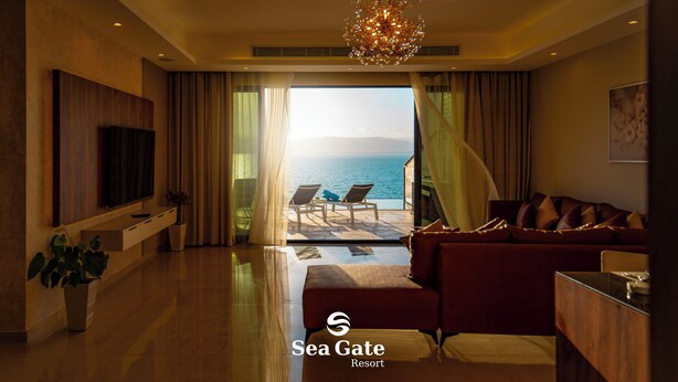 A modern living room with a large TV, a sofa, and a view of the sea.
