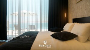 A hotel room with a bed, a view of the sea through sheer curtains, and a chair by the window.