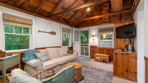A cozy cabin interior with a wooden ceiling, a sofa, a television, and a dining area. - Lakefront Cottage Retreat: 3BR w/ Fire Pit, BBQ & Dock (Plymouth)