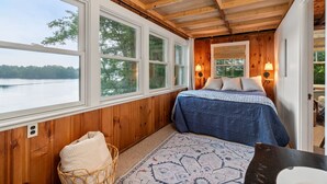 A bedroom with a large window, wooden ceiling, and a bed with a blue blanket. - Lakefront Cottage Retreat: 3BR w/ Fire Pit, BBQ & Dock (Plymouth)