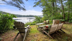 A lakeside outdoor seating area with a wooden Adirondack chair, a green sofa, and a table. - Lakefront Cottage Retreat: 3BR w/ Fire Pit, BBQ & Dock (Plymouth)