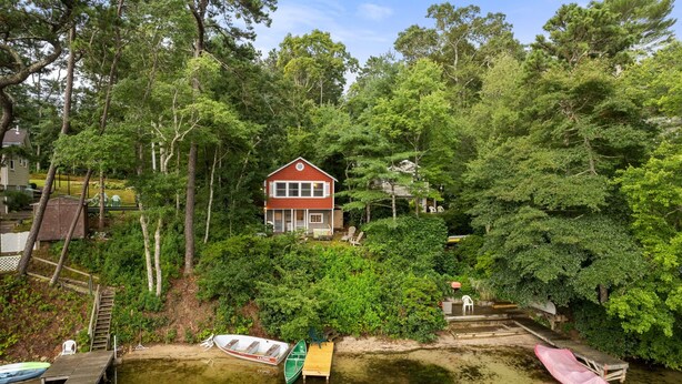 A house surrounded by dense forest, with a dock and boats in the foreground. - Lakefront Cottage Retreat: 3BR w/ Fire Pit, BBQ & Dock (Plymouth)